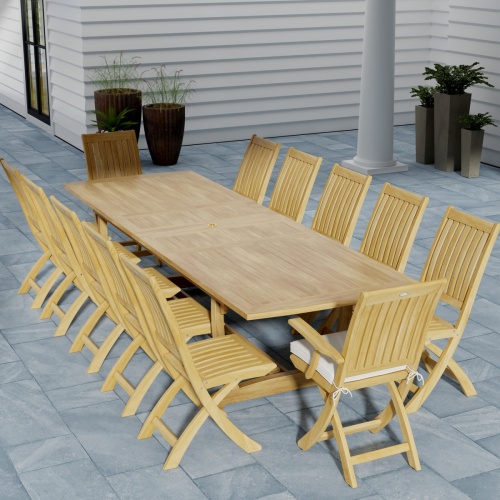 70059 Grand Barbuda 13 pc Teak Dining Set angled end view on patio with optional seat cushions and 6 potted plants against the house wall in the background