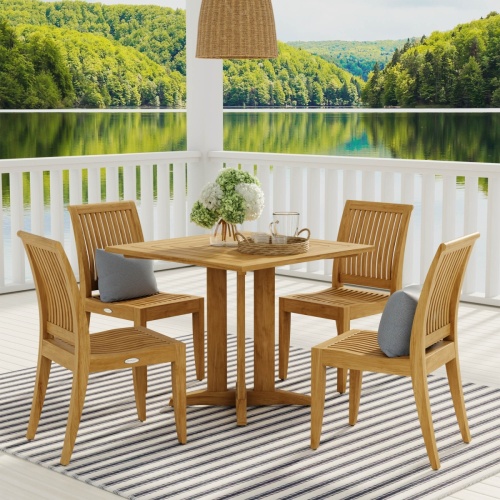 70292 Pyramid Laguna 5 piece teak Dining Set with 2 optional throw pillows with woven tray with water pitcher and glasses and vase of  hydrangeas on a patio with lake view in background