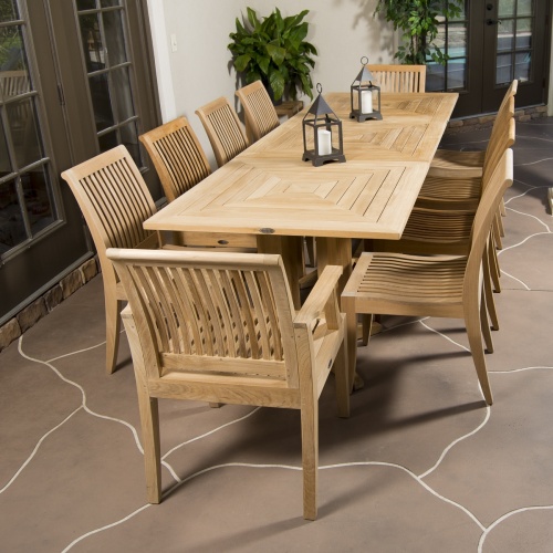 70434 Pyramid teak Rectangular Table Dining Set showing 2 black metal pillar candle holders with white candles on table on stone patio 2 potted trees end angled view with house in back 