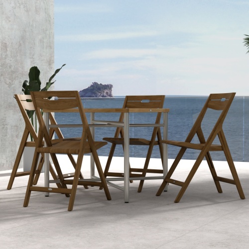 70450 Surf Odyssey Folding Dining Set of Odyssey Bistro Table and 4 Surf Side Chairs in side view on a stone patio with the ocean and blue sky in the background