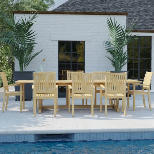 70759 Sussex Veranda 9 pc Teak Patio Dining Set in side view on pool deck behind a pool with house with windows and 2 potted plants in background 