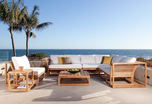 11800RFDP Maya teak lounge set with bowl of apples a potted plant and magazine on table shelf on concrete patio surrounded by two palm trees and plants with ocean and blue sky background