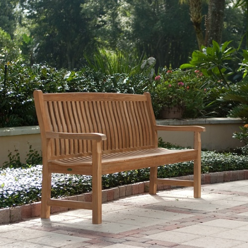 13618 Veranda Teak 5 foot long Bench on concrete stone patio with shrubs and flowers in background