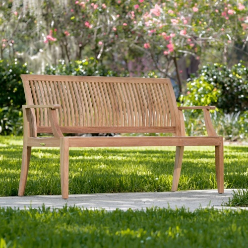 13811 Laguna 5 foot Teak Bench on concrete walkway showing grass lawn in front and behind bench with landscape shrubs and trees in background   