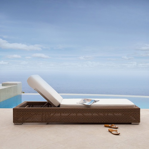 30002dp Malaga synthetic wicker chaise lounger with cushions side profile with magazine lying open on chaise and sandals next to chaise on patio with pool and ocean background