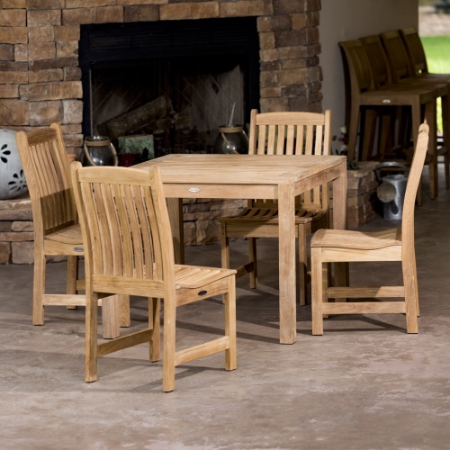 70424 Veranda teak 5 piece square Bistro Set of 4 teak side chairs and 36 inch square dining table on concrete patio with fireplace in background