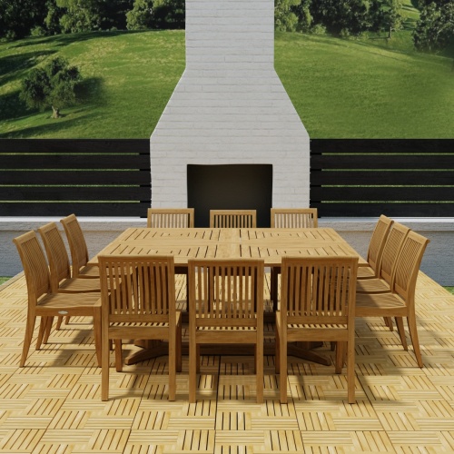 70435  Pyramid 14 pc Teak Dining Set on Teak Parquet floor deck in front of an outdoor fireplace with privacy wall and green lawn in background