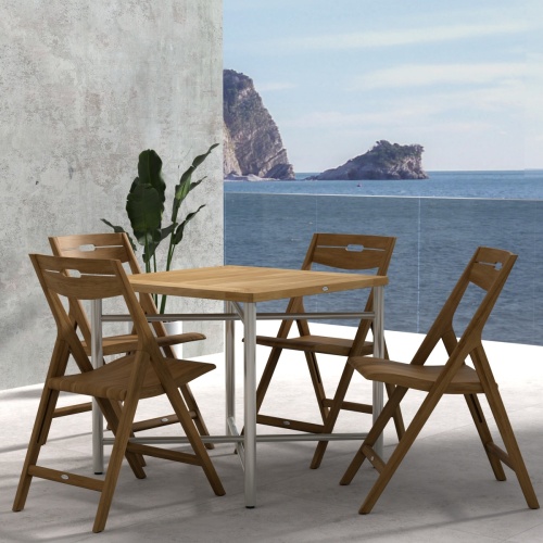 70450 Surf Odyssey Folding Dining Set of Odyssey Bistro Table and 4 Surf Side Chairs in angled side view on a stone patio with the ocean and blue sky in the background