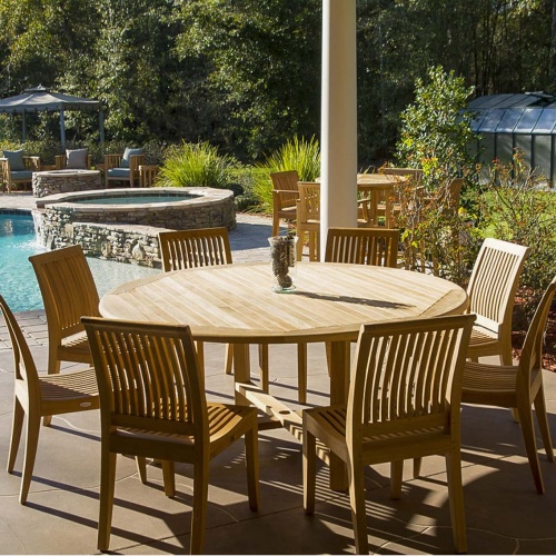 70493 Buckingham Laguna teak 9 piece Dining Set of 8 side chairs and 6 foot round table with vase of pinecones on stone patio with pool in back surrounded by landscape plants 