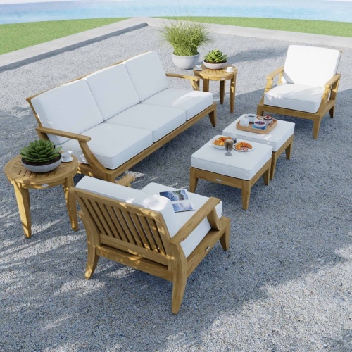 70871 Laguna 7 pc Conversation Set aerial view on a stone rock terrace with 3 potted plants and magazine and plates on ottoman surrounded by grass lawn with water view in background 