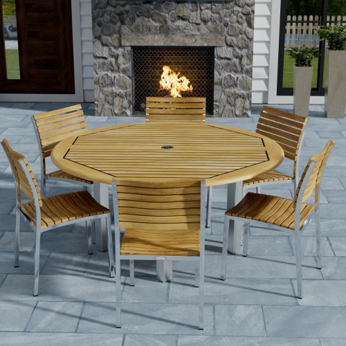 70439 Vogue Dining Set for 6 of Vogue Teak and Stainless Steel 60 inch Round Dining Table and 6 Vogue Side Dining Chairs angled top view with an outdoor fireplace in the background 