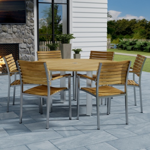 70442 Vogue Teak 7 pc Dining Set showing Vogue 60 inch Round Dining Table and 6 Dining Chairs side view on patio with window and fence with trees in background
