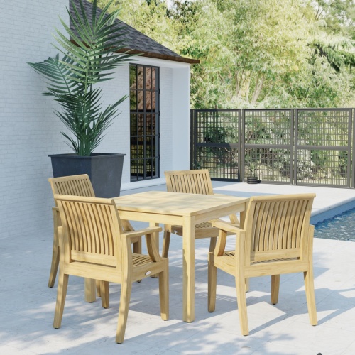 70555 Laguna 5 pc Square Dining Set of Bistro 36 inch Square Teak Dining Table and 4 Laguna Dining Armchairs in corner view on patio next to a house and fence in the background 