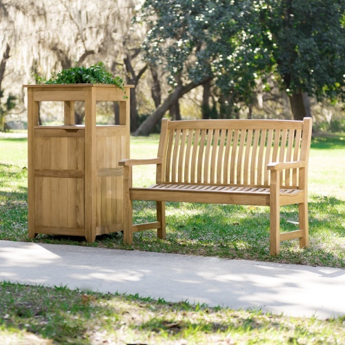 13218 Veranda Teak 4 foot Bench beside teak trash receptacle on grass field with concrete walkway in front and trees in background