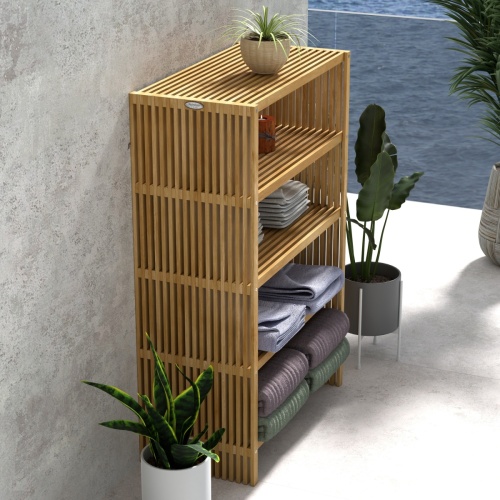 18221 Teak 48 inch Storage Shelf in angled aerial side view next to potted plants against a wall with a potted plant on top of shelf and folded towels on the lower shelves with ocean in back