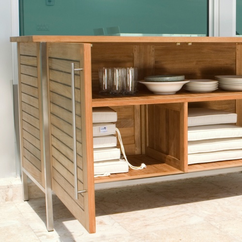 28225RF Vogue teak and stainless steel Sideboard on outdoor patio with sideboard doors open displaying storage area with dishes and seat cushions against glass windows