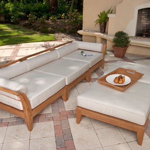 thumbnail image of 70102 Aman Dais 3 pc Sofa Set cushioned with magazine and two optional ottomans with plate of pears on teak tray set on patio with fireplace two plants grass and treed background 