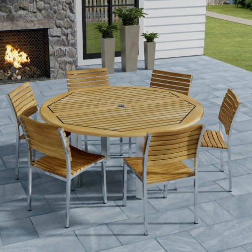 70439 Vogue Dining Set for 6 of Vogue Teak and Stainless Steel 60 inch Round Dining Table and 6 Vogue Side Dining Chairs angled aerial view with an outdoor fireplace in the background 
