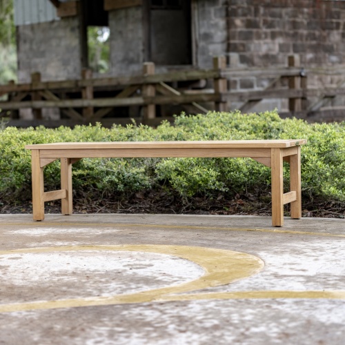 13929 Veranda teak 5 foot long Backless Bench side view on stone patio with bushes and concrete building in background