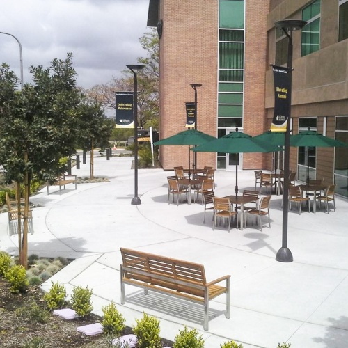 23200 Vogue 5 foot Teak and Stainless Steel Bench aerial view on concrete patio with umbrellas and various patio furniture in background