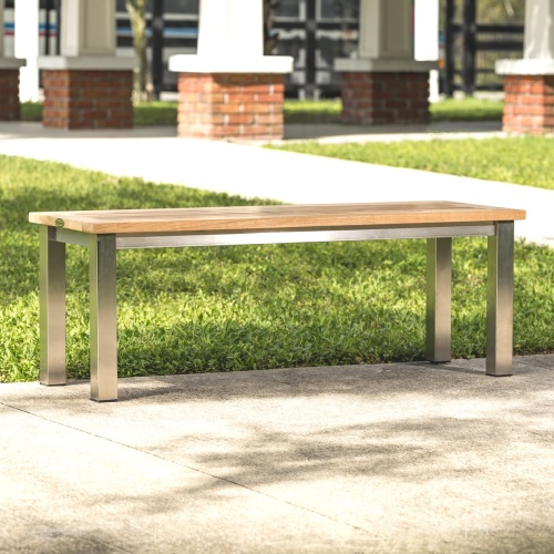  23940 Vogue teak and stainless steel 4 foot backless bench on concrete walkway with grass and house in background