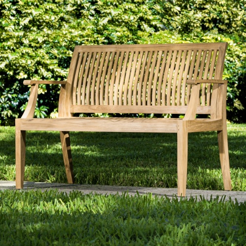 13810 Laguna 4 foot Teak Bench front angled view on concrete walkway with bushes in background