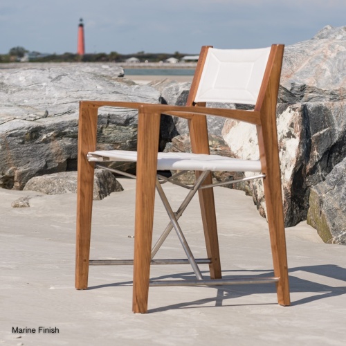 12915F Odyssey Teak and 316L Stainless Steel Chair facing left view on sandy beach by boulders