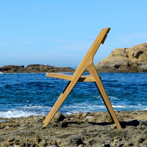 70474 Surf Barbuda folding side chair on sandy beach left side facing ocean with rocks and blue sky background