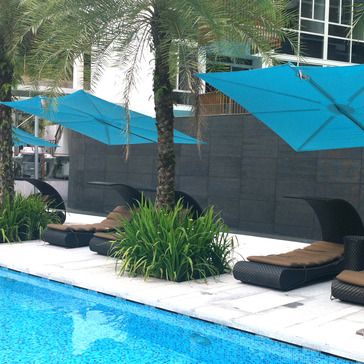 image of SPS2590SFB Spectra umbrella showing 3 in blue canvas on concrete patio by a pool with palm trees and loungers in background