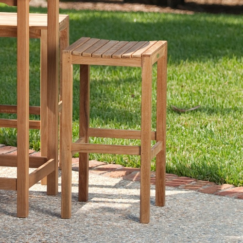 70533 Somerset Laguna teak backless barstool closeup of side view on white brick patio with grass field in background