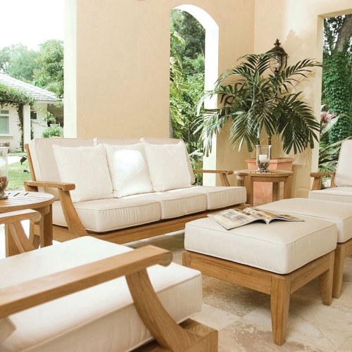 70871 Laguna 7 pc Conversation Set on travertine tile patio open magazine on ottoman two pillar candles on side table potted palm tree with landscape plants trees and house in background