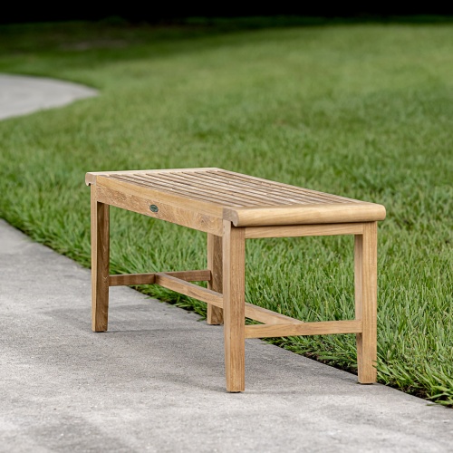 13915 Laguna 4 foot long teak Backless Bench on concrete walkway with grass in background