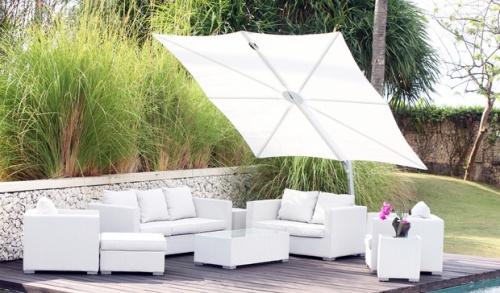 SP25100SET Spectra Solo Umbrella and Paver Base with white canopy over white sofa set on wood deck stone railing behind deck tall grass shrubs and grass in background