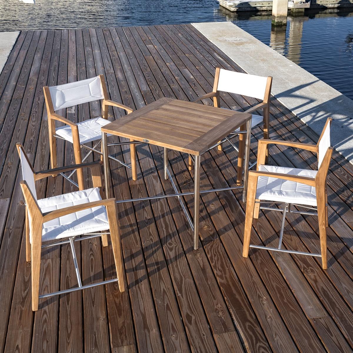 An image of 70459 Odyssey 5 Piece folding teak and stainless steel dining set of  Odyssey 32 inch square dining table and 4 Odyssey folding chairs on a boat dock next to a boat marina.
